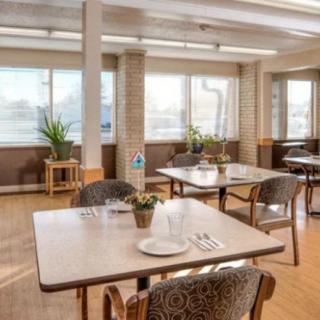 A well-lit dining area with neatly arranged tables and chairs, adorned with plants.