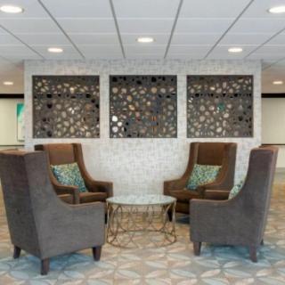 A modern lobby seating area featuring four brown chairs and a glass coffee table with decorative wall panels.