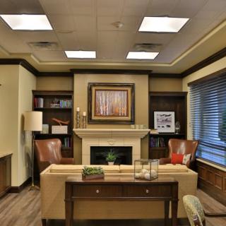 A well-appointed office space featuring a central desk, flanked by bookshelves and comfortable chairs with artwork above the fireplace.