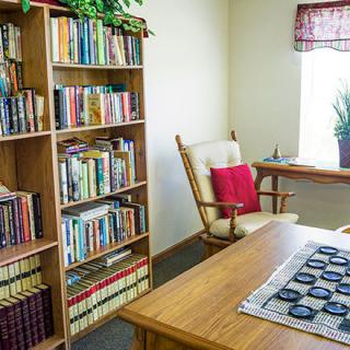 A cozy reading room with a bookshelf, rocking chair, and desk by the window.