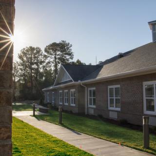 A building with a brick exterior illuminated by bright sunlight, surrounded by a green lawn and trees.