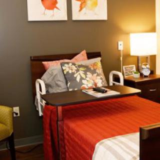 A well-appointed hospital room with a cozy bed, colorful pillows, and a bedside table equipped with a lamp.