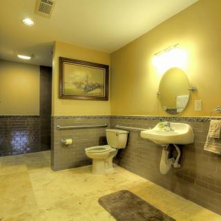 A spacious and well-lit bathroom featuring a sink, toilet, mirror, and decorative wall art.