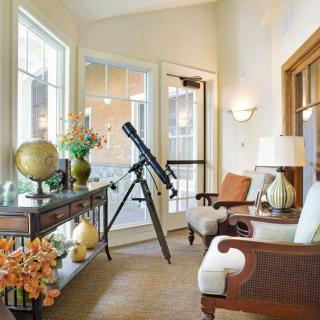 A cozy living room with a telescope by the window, featuring comfortable seating, decorative items, and a globe.
