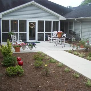 A cozy backyard patio with a screened porch, outdoor furniture, and landscaped garden.