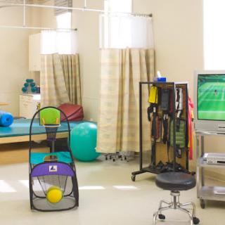 A therapy room equipped with various exercise and rehabilitation tools, including colorful balls and a monitor for treatment guidance.