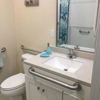 A bathroom with safety handrails, featuring a sink, toilet, and mirror.