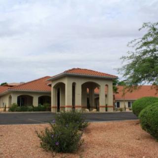 A desert-style building with arched entrance and red-tiled roof surrounded by shrubs.