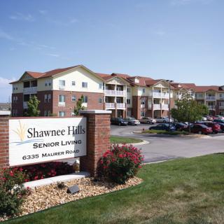 A large residential building with a sign reading 'Shawnee Hills Senior Living' and a parking lot in the foreground.