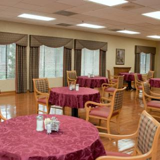 A spacious dining area featuring tables with red tablecloths and comfortable chairs, illuminated by natural light from large windows.