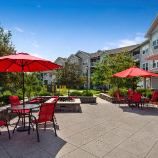 An outdoor patio area with red tables and chairs under umbrellas at an apartment complex.