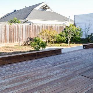 A backyard featuring a wooden deck and garden area, enclosed by a wooden fence.