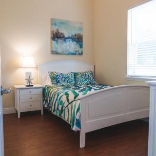 A cozy bedroom with a white bed frame, colorful bedding, and a nightstand with a lamp.