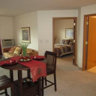 A cozy apartment interior featuring a living room with a dining area and an adjoining bedroom.