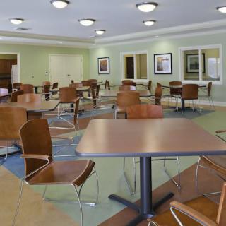 An empty cafeteria with modern tables and chairs, softly lit with ceiling lights.