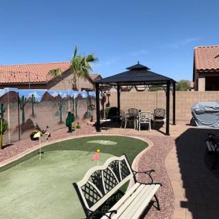 A sunny backyard featuring a putting green, gazebo, and bench in a desert landscape.