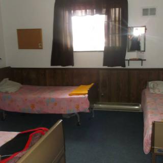 A simple room with two single beds, a window with curtains, and a mirror on the wall.
