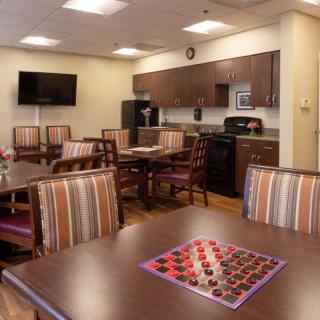 A cozy common area with a kitchenette, tables with seating, and a checkers board ready for play.