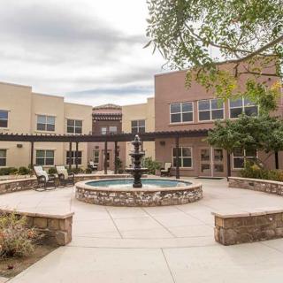 A peaceful courtyard featuring a central fountain, surrounded by a building and outdoor seating.