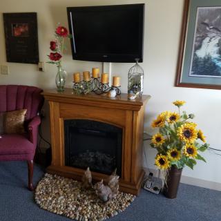 A cozy living room with a decorative fireplace, sunflowers, and artwork on the wall.