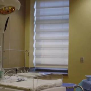 A hospital room with a bed and medical equipment near a window with blinds.