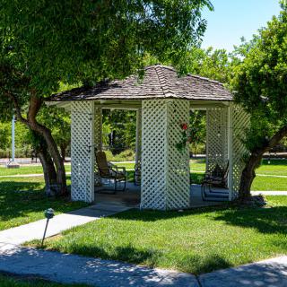 A charming lattice gazebo surrounded by greenery in a sunny park setting.