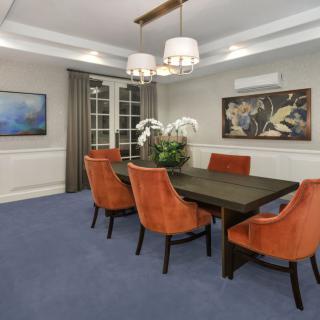 A modern dining room featuring orange chairs around a dark table, adorned with a central plant and illuminated by elegant chandeliers.