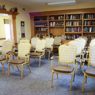 An empty library room with chairs arranged in rows and bookshelves lining the walls.
