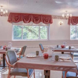 An empty dining room with neatly arranged tables and chairs, adorned with red curtains and soft lighting.