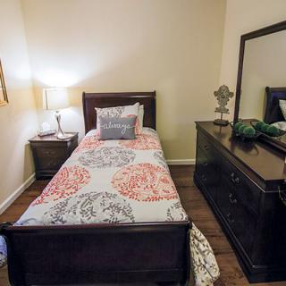 A cozy bedroom with a single bed, nightstand, and dresser featuring a mirror.