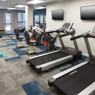 A modern gym featuring treadmills and elliptical machines, equipped with wall-mounted televisions.