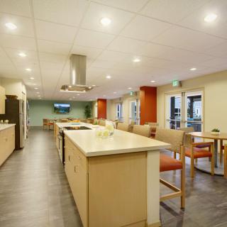 A spacious, modern kitchen and dining area with an island counter surrounded by chairs and bright lighting.