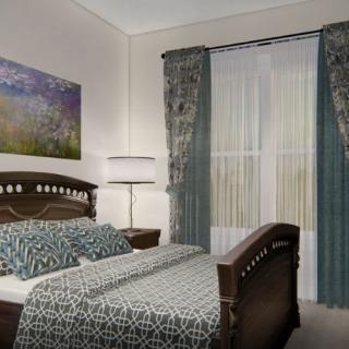 A cozy, elegantly designed bedroom featuring a double bed with patterned bedding, decorative curtains, a standing lamp, and artwork on the wall.