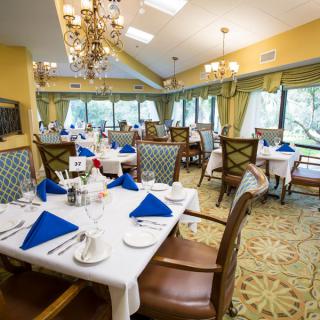 An elegant dining room with neatly arranged tables, featuring blue napkins and chandeliers.