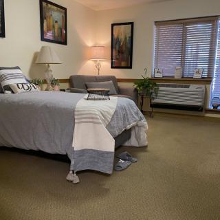 A cozy bedroom with a neatly made bed, a lamp, and a comfortable chair beside the window.