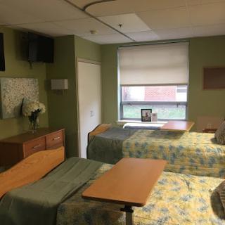 A view of a hospital patient room equipped with two beds, a television, and a window.