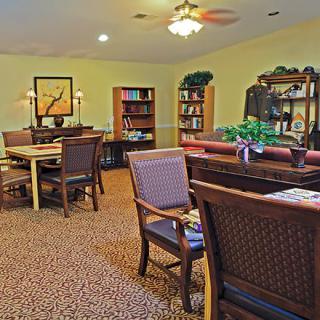 A cozy living room with tables and chairs, surrounded by bookshelves and warm lighting.