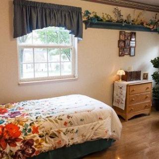 A cozy bedroom with a single bed featuring floral bedding, a window with curtains, and a wooden dresser.