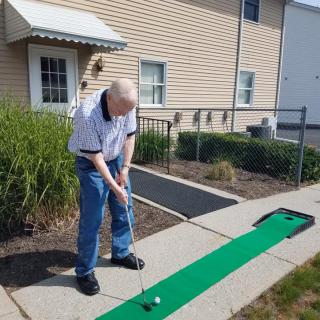 A person playing mini golf outdoors on a green mat.