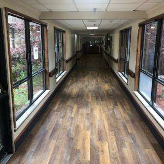 A well-lit corridor featuring windows on either side and a wooden floor, creating an inviting atmosphere.