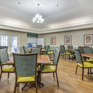 A well-lit dining area with multiple tables and chairs arranged neatly under a chandelier.