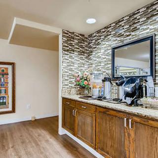 A modern coffee station with wooden cabinets and a stylish tiled backsplash, featuring a mirror and hardwood flooring.
