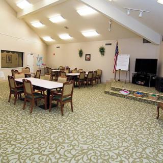A community meeting room with tables, chairs, a television, and an American flag.
