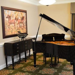 A music room featuring a grand piano and a painting of horses on the wall.