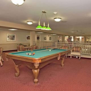 A spacious billiard room with a pool table and green overhead lighting, featuring comfortable seating and decor.