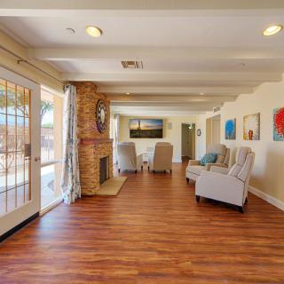 A spacious living room with hardwood floors, featuring a cozy fireplace and comfortable armchairs alongside large windows and colorful artwork.