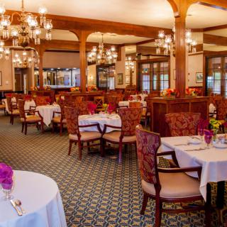 An elegant restaurant dining room with beautifully set tables and ornate chandeliers.