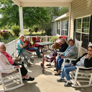 A group of elderly individuals relaxing on a porch in rocking chairs, enjoying the outdoor setting.