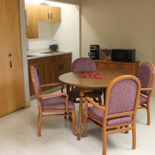 Cozy dining area with a wooden table and purple upholstered chairs adjacent to a small kitchenette.