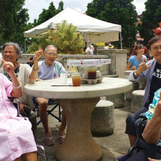 A group of elderly people enjoying drinks together at a stone table in an outdoor setting.